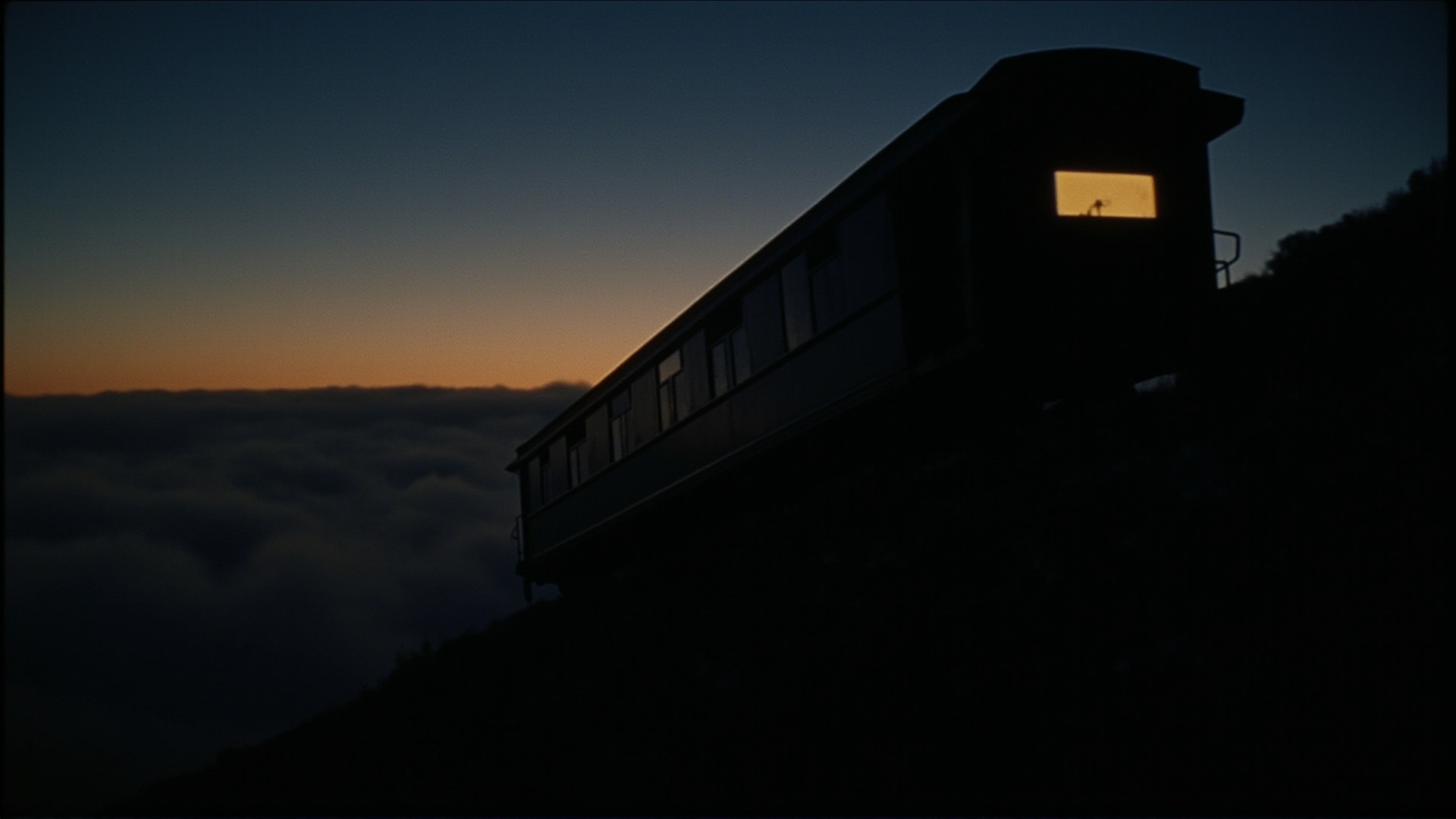 The silhouette of an inclined-railway car on a hillside trestle at dusk, one lit window
